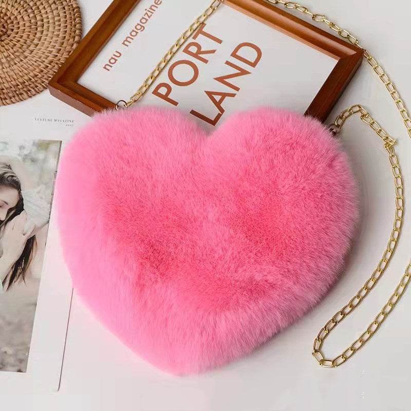 Pink heart shaped soft plush handbag for women with gold chain strap on white table