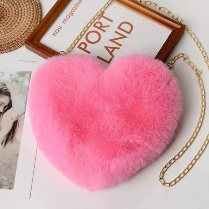 Pink heart shaped soft plush handbag for women with gold chain strap on white table