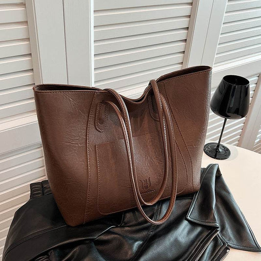 Brown retro shoulder bag for women with long straps displayed on black leather jacket and white table