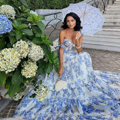 Woman in a blue floral dress holding an umbrella with hydrangeas in the foreground.