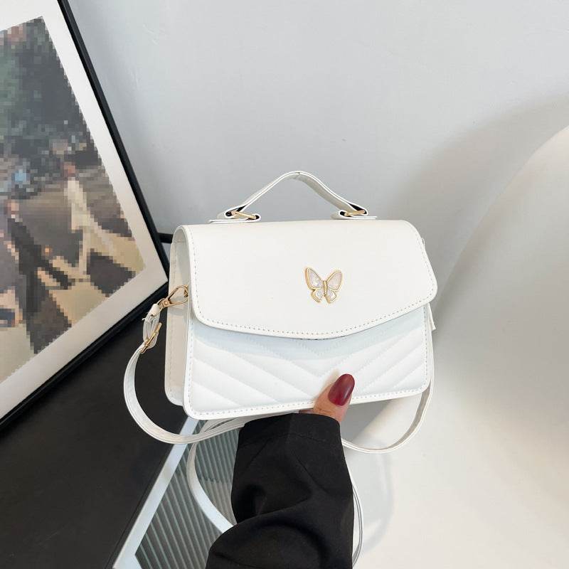 White quilted flap bag with gold butterfly accent, top handle and strap, versatile crossbody purse for women