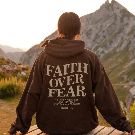Person wearing Faith Over Fear hoodie from Holy Mango Store sitting outdoors with mountains in background