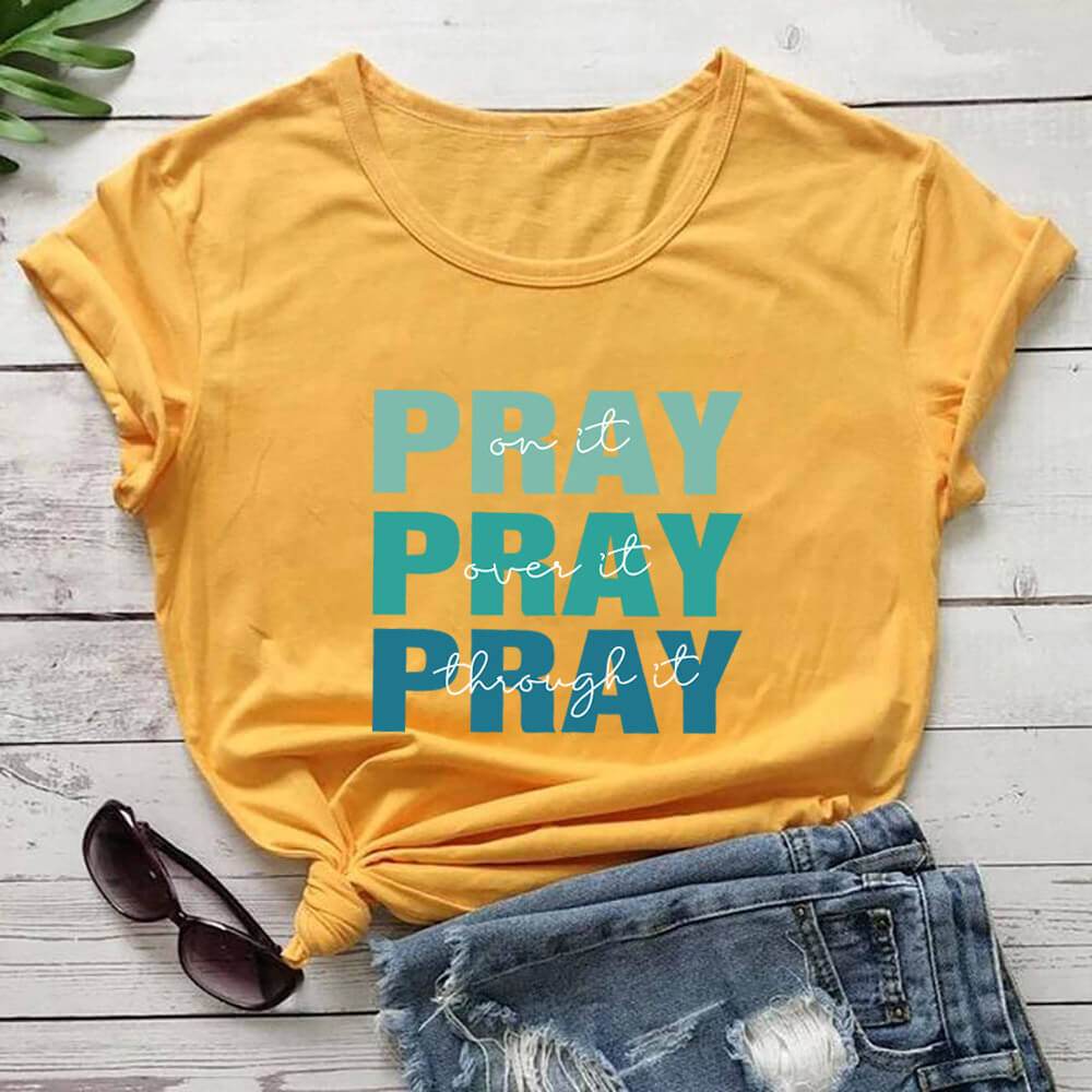 Yellow faith themed t shirt with blue Pray text and inspirational message styled with denim shorts and sunglasses