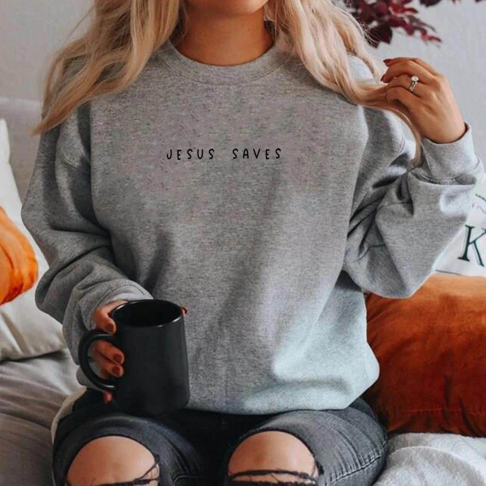 Gray Jesus Saves sweatshirt worn by person holding black mug sitting on couch with ripped jeans